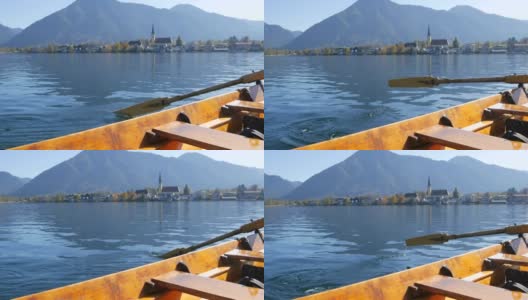 在巴伐利亚泰根塞湖风景如画的教堂的背景下，一个木船船夫拿着桨把人们带到另一边高清在线视频素材下载