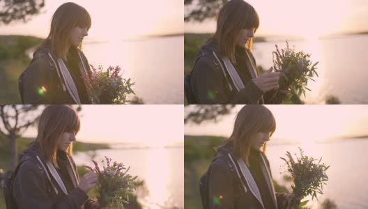 美丽的年轻女子拿着一束野花在日落的海岸上高清在线视频素材下载