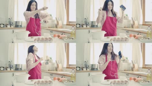 年轻的亚洲女人听音乐与手机和跳舞在厨房。高清在线视频素材下载