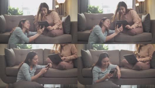 两个年轻的亚洲女性朋友坐在沙发上，用她的手机在家里高清在线视频素材下载