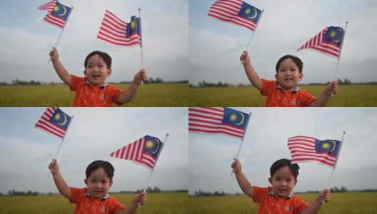 马来西亚独立日，一个亚洲华人小男孩在帕迪球场挥舞着马来西亚国旗，享受着清晨的阳光，感到自豪和快乐高清在线视频素材下载