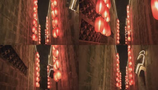 晚上在古庙狭窄走廊的石墙中间往前走。点燃了红灯笼，四处悬挂着照明灯。传统装饰，节日庆典高清在线视频素材下载