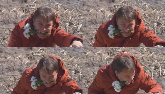 一名身穿羽绒服的年轻人在极端条件下为心爱的人收集了一束春天的鲜花，然后用嘴叼着。带着安全绳的人爬到岩石上制造惊喜，从上往下看。高清在线视频素材下载