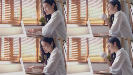 假日休息的亚洲女性白种人微笑着坐在卧室的窗户边看平板和喝咖啡，阳光透过窗户照射进来高清在线视频素材下载