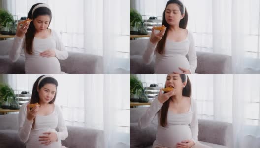 亚洲妇女怀孕期间在家里的沙发上吃不健康的披萨。垃圾食品高清在线视频素材下载
