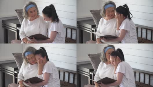 亚洲年轻的女儿和年长的母亲在家里一起读书。年轻女子读人寿保险单给老妈妈听高清在线视频素材下载