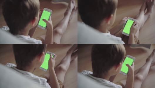 小男孩在手机上看内容。绿屏模型。带着智能手机的孩子的后视图高清在线视频素材下载