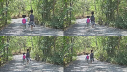 非裔美国可爱的小妹妹在森林里徒步旅行。两个黑人女孩在野外旅行。一群小学生背着书包，手牵着手在公园里散步。高清在线视频素材下载