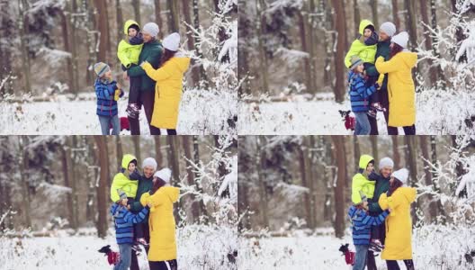 爱的家庭-妈妈，爸爸，女儿和儿子拥抱在白雪覆盖的树的背景高清在线视频素材下载