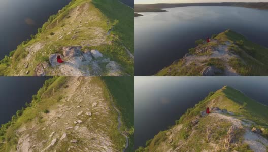 空中飞行，一对相爱的情侣站在悬崖边靠近水。穿着红色裙子的女人。人黑。日落高清在线视频素材下载