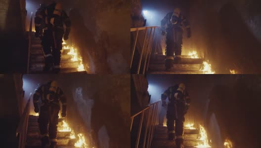 两名强壮的消防员在燃烧的大楼里上楼。楼梯被明火燃烧。在缓慢的运动。高清在线视频素材下载