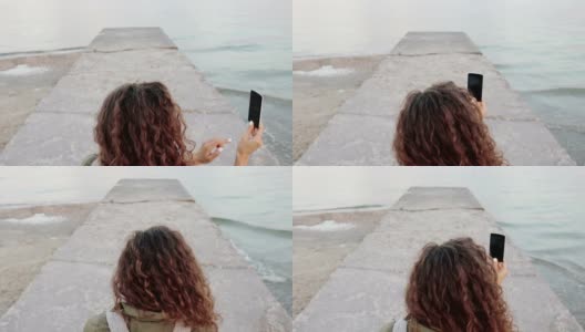 年轻的卷发黑发在手机上拍摄海景，从后面看，特写高清在线视频素材下载