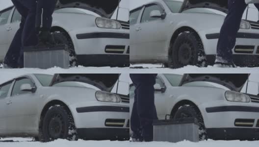 冬天，人们从覆盖着积雪的地面上举起汽车电池，把它送到汽车上。一个在下雪时修理坏了的汽车。车辆故障或问题。引擎盖或引擎盖抬起高清在线视频素材下载