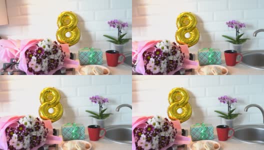 厨房桌上摆着一束春天的鲜花和金色的气球，还有礼品盒和早餐。光北欧风格。母亲的一天。3月8日是国际妇女节高清在线视频素材下载