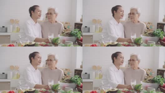 爱的时刻，亚洲妈妈亲吻在厨房准备早餐，蔬菜，水果与大女儿，享受周末活动高清在线视频素材下载
