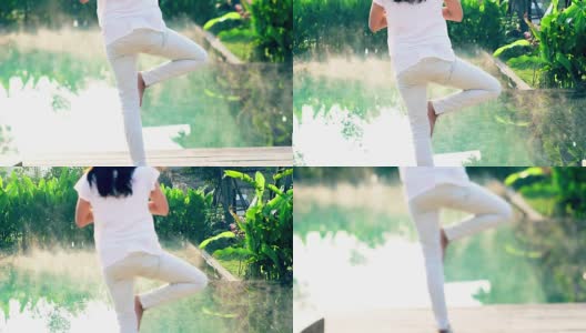 亚洲女孩锻炼瑜伽旁边的健康水疗池在绿色的背景和晨雾的慢动作拍摄高清在线视频素材下载