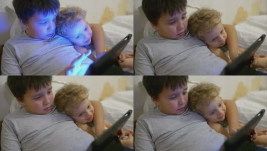 两个男孩在床上拿着触摸板。一个玩游戏高清在线视频素材下载