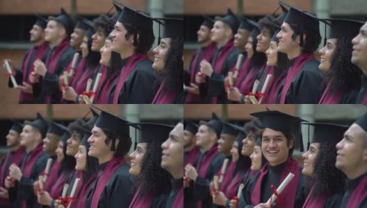 在毕业典礼上，一名年轻人看着镜头，而其他同学则站成一排看着别处高清在线视频素材下载