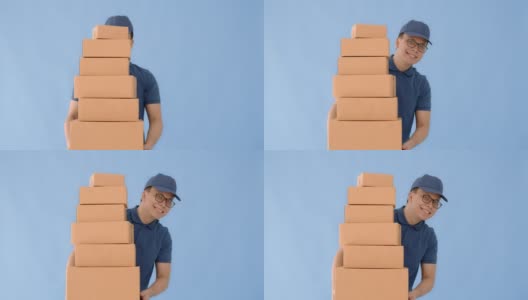 亚洲快乐快递员戴着一顶帽子和一件蓝色衬衫携带纸包盒子孤立在蓝色背景与微笑的脸。邮政投递服务的概念。高清在线视频素材下载