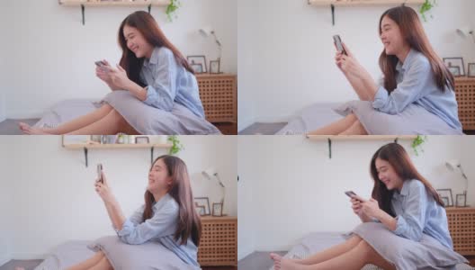 侧面的漂亮和美丽的亚洲女孩使用手机和坐在床上的卧室与幸福的情绪高清在线视频素材下载