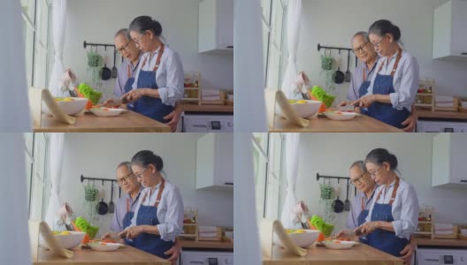 爱亚洲的老夫妇穿着围裙在厨房做饭。英俊强壮的老爷爷奶奶戴着眼镜，在家享受退休生活活动。家庭关系的概念。高清在线视频素材下载