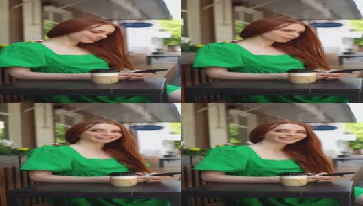 在阳光明媚的夏日，微笑的年轻女子的垂直肖像使用浏览手机坐在餐桌咖啡杯在户外咖啡馆露台。高清在线视频素材下载
