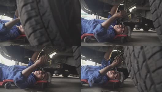 小车从侧面拍摄:亚洲高级汽车技师在车下工作高清在线视频素材下载