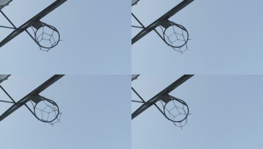 在篮球场上，一个篮球穿过一个有金属链网的篮筐。背景是天空和云彩高清在线视频素材下载