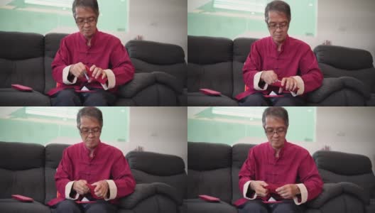 中国新年期间，亚洲华人微笑的老人在生活大厅把钱放进红包高清在线视频素材下载