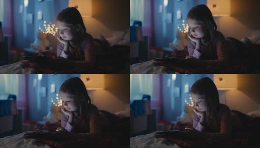 可爱的小女孩晚上在她的房间里，躺在床上使用智能手机。她的夜灯打开了。高清在线视频素材下载