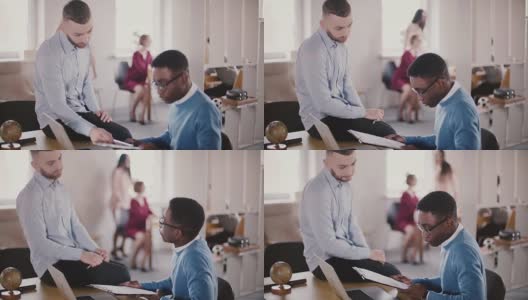 自信的年轻男性CEO商人正坐在办公室的桌子上，帮助他的非裔美国同事共同工作高清在线视频素材下载