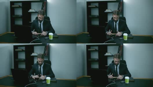 紧张的商人坐在办公室里的笔记本电脑后面，男员工看着手机，生气，慢动作高清在线视频素材下载