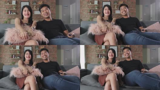 一对亚洲夫妇在度假的时候坐在家里的沙发上看电视，开心地笑着。高清在线视频素材下载