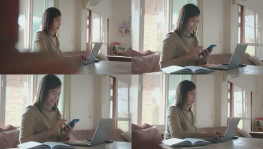 年轻的亚洲女子在电脑上打字，并收到来自智能手机的信息与微笑。在家工作的女性员工。高清在线视频素材下载