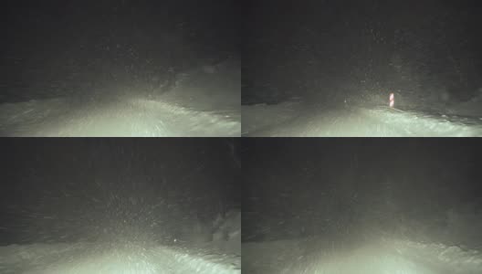 司机POV在积雪覆盖的道路上行驶，初雪飘落。被前灯和雪照亮的路。高清在线视频素材下载