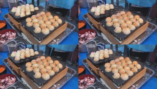 在日本的街头小吃市场，厨师从章鱼烧锅中手拿起日本小吃章鱼烧，并将其装进盒子里，在夏季节日时出售。男子烹饪什锦传统日本肉丸。高清在线视频素材下载