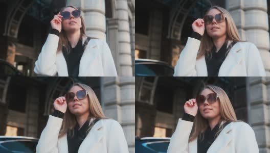 一个戴着眼镜、穿着白色外套的女孩站在市中心一家酒店的背景下，调整着自己的眼镜高清在线视频素材下载