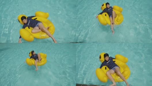 快乐的亚洲男孩放松在黄鸭橡皮筏在游泳池与家人度假，生活理念。高清在线视频素材下载