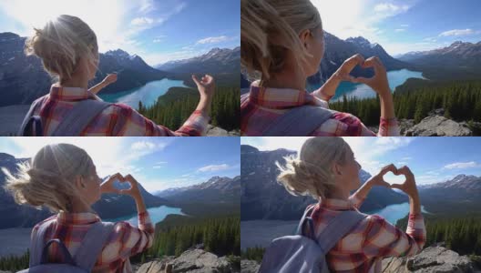 一个年轻女子站在湖上的山顶上，用手指做了一个心形的框架高清在线视频素材下载
