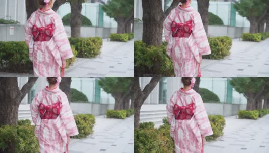 快乐年轻美丽的亚洲女人女孩穿着粉红色的传统日本和服走在市中心的街道上，看着远离东京城市，日本的4K后视图高清在线视频素材下载