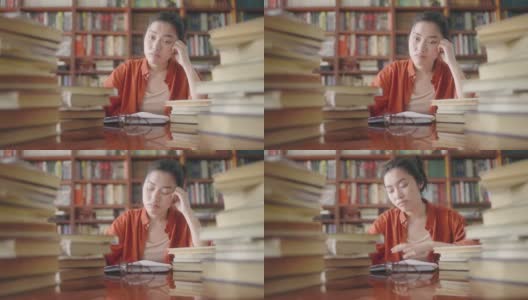 心烦意乱的亚洲女学生坐在书堆后面，学业压力高清在线视频素材下载