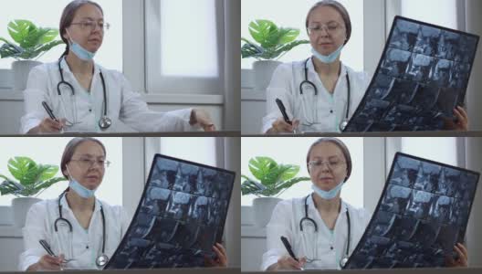 一名戴眼镜的白人女医生在诊所的办公桌前检查x光照片。放射科医师分析部分头部CT扫描并记录结果高清在线视频素材下载