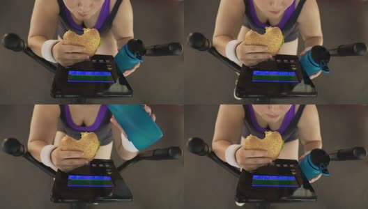 胖女孩过度吃汉堡和喝水，同时骑健身自行车高清在线视频素材下载