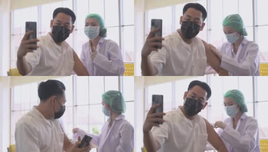 图为一名亚洲男子在诊所或医院接种新冠疫苗时通过手机自拍，护手注射疫苗以获得免疫力以保护病毒。人们戴着防护口罩。高清在线视频素材下载