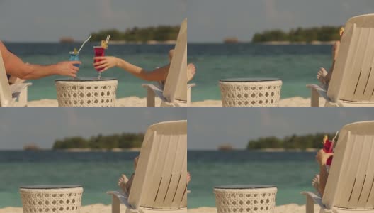 年轻的家庭夫妇日光浴和喝彩色鸡尾酒在热带海滩。情侣在蜜月异国度假躺在海边的躺椅上的阳光度假高清在线视频素材下载