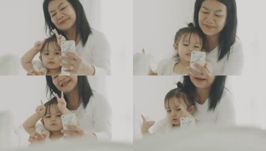 泰国可爱的小女孩和她的妈妈在卧室用智能手机自拍的现代生活方式高清在线视频素材下载