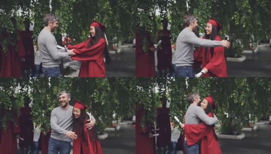 一位慈爱的父亲在毕业典礼上祝贺他的女儿，人们在户外拥抱和欢笑，背景中可以看到其他毕业生。高清在线视频素材下载
