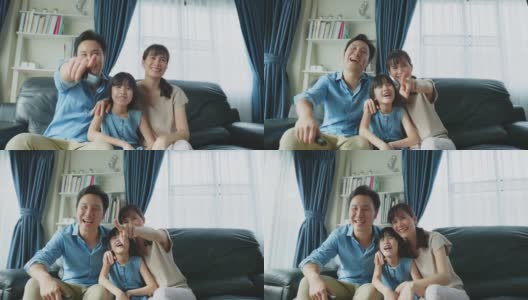 幸福的亚洲家庭呆在客厅里一起看电视电影。父亲和母亲花闲暇时间与小女孩女儿坐在沙发上，看动画片，在家里一起欢笑。高清在线视频素材下载