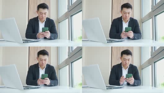 年轻的亚洲上班族坐在办公室里，用智能手机聊天发短信高清在线视频素材下载
