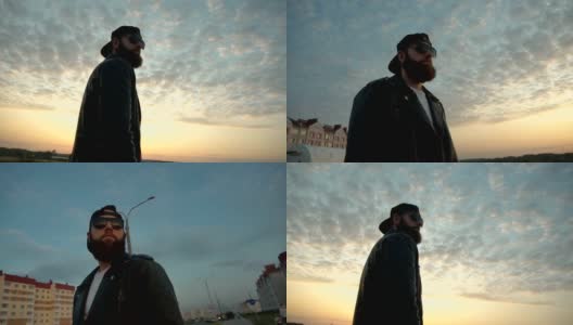 英俊时尚的白人男子模型在黑色眼镜与胡子看着在城市的一个阳光日落的背景远处，背景。慢动作高清在线视频素材下载